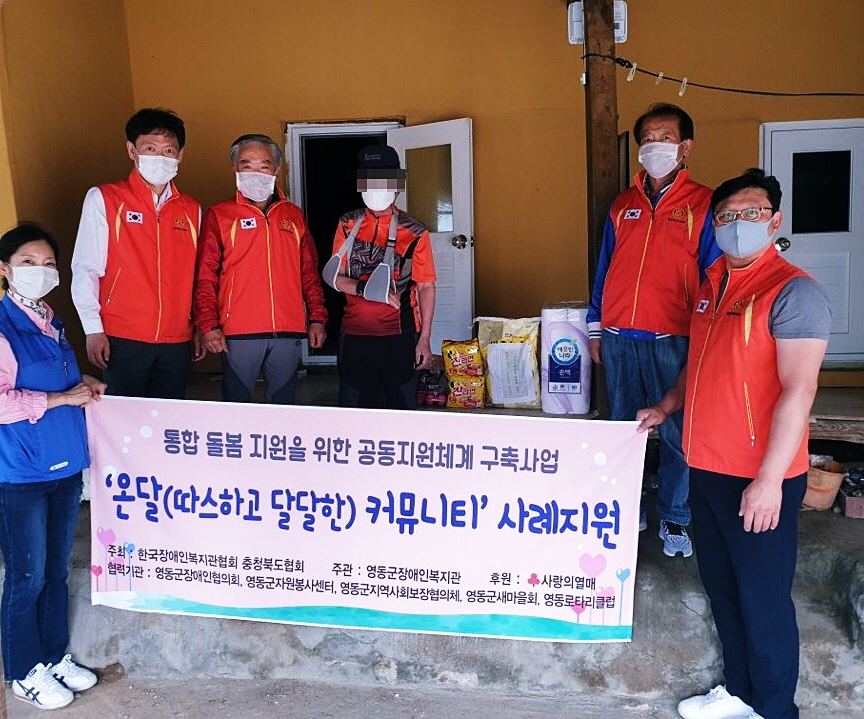 통합돌봄 지원을 위한 공동지원체계 구축사업의 하나로 사례지원을 한 가정에서 후원자와 대상자분들의 기념 촬영을 한 사진입니다. 사진의 내용은 6명이 서 있고 앞에 두명은 앞에서 온달커뮤니티 사례지원 플랜카드를 양쪽에서 들고 있는 사진입니다.